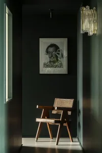 A minimalist interior design featuring a wooden chair and a black and white portrait hanging on a dark green wall.
