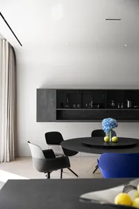 A minimalist dining room with a black concrete table and chairs, featuring blue flowers and green apples on a lazy Susan.