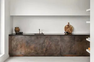 A minimalist kitchen featuring wooden cabinets, a black countertop, and a minimalistic design.