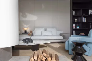 A modern living room featuring a light-colored couch, a table lamp, and a tall bookshelf filled with books.
