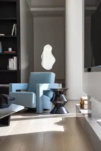 A modern living room with a blue upholstered armchair, a black geometric table, and a bookshelf filled with books and decorat