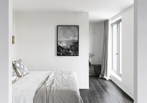 A minimalist bedroom with a white bed, gray walls, and a large window.