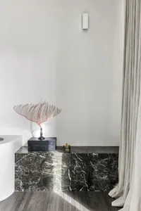 A modern minimalist bathroom featuring dark marble stone with a sleek, geometric artwork and a white sink.