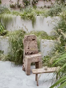 A rustic wooden chair and table in an outdoor garden setting surrounded by green foliage and plants.