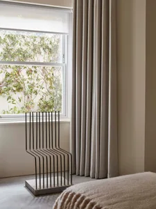 A minimalist bedroom featuring grey curtains and a modern metal sculpture by the window.