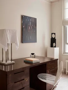 Modern minimalist home office with a wooden desk featuring abstract art and a sleek, white chair.