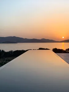 A minimalist swimming pool with an infinity edge overlooks a sunset view over the sea and mountains.