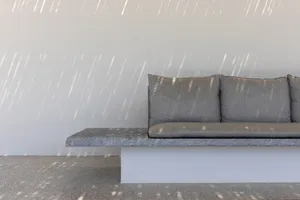 Modern living room featuring a concrete sofa with cushions on a white base against a white wall, with sunlight casting shadow