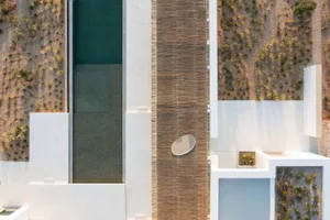 A modern, minimalist swimming pool deck made of concrete with a wooden walkway bordered by desert plants.