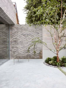 Modern minimalist outdoor living space featuring a sleek metal chair, a lush tree, and a minimalist wall design with concrete