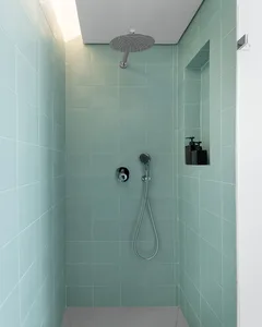 A modern bathroom with teal ceramic tiles, featuring a standing shower with a ceiling-mounted showerhead and handheld shower.