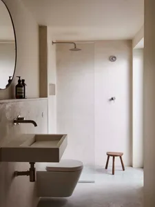 A modern bathroom with concrete walls, a wall-mounted sink, a walk-in shower, and a small wooden stool.