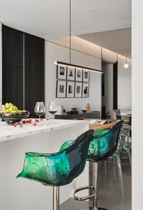 A modern kitchen featuring a marble countertop with green and blue glass bar stools and wine glasses.