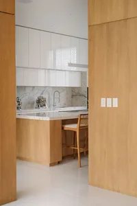 Modern kitchen featuring white marble countertops and backsplash with wooden cabinets and flooring.