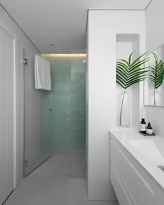 Minimalist bathroom with green glass tile shower, white tiles, and concrete floor, featuring a floating vanity and a leafy pl