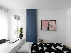 A minimalist bedroom with a black and white patterned bedspread, a blue panel, and a window with white curtains.