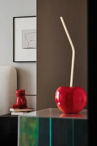 A modern, red ceramic apple with a gold stem placed on a glass surface, surrounded by a minimalist decorative setting.