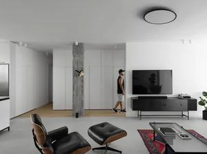 Minimalist living room with concrete and white furniture, featuring a black TV stand and a black leather chair with ottoman.