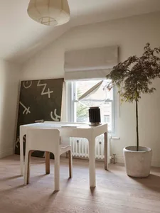 A modern home office with minimalist design, featuring a white desk, chair, and a lamp with a white shade.