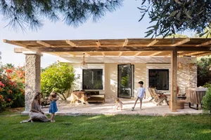 A modern farmhouse-style residential exterior with a wooden pergola and a family playing on the patio