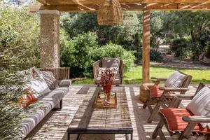 Outdoor living space featuring wooden furniture, concrete columns, and lush greenery in the background.