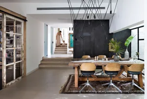 A modern dining room with a wooden table, concrete floor, and glass chandelier.