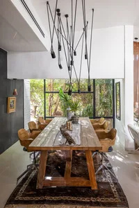 A modern industrial dining room featuring a wooden table and chairs, set against a backdrop of large windows overlooking a gr