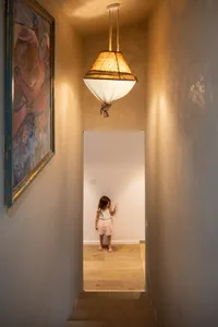 A young girl in a tutu skirt plays under a hanging lamp in a children's room with wooden stairs and walls.