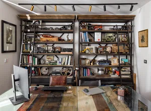 A home office with wooden shelves filled with books, cameras, and vintage items.