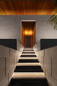A modern interior staircase with concrete steps and illuminated risers, featuring a wooden ceiling.
