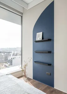 A modern bedroom featuring a blue accent wall with sleek, black metal shelves and a large window overlooking a cityscape.