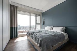 A cozy modern bedroom with a bed, fabric window curtains, and a view of the city.