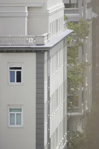 一座現代公寓大樓，白色建築搭配混凝土陽台，街道兩旁綠樹成蔭。