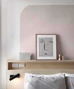 A minimalist bedroom with a wooden headboard and a framed abstract face drawing on the wall.
