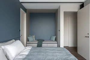 A minimalist bedroom featuring a comfortable seating nook with textured soft furnishings, including a grey bedspread and cush