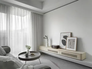 Neutral-toned minimalist living room with white curtains, round coffee table, and abstract artwork on the wall.