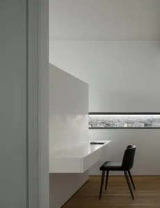 A minimalist desk with a white surface in a well-lit room with a view of the cityscape.