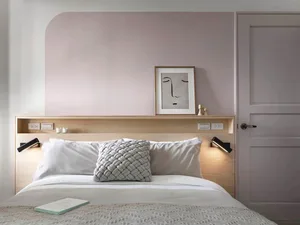A modern minimalist bedroom with a wooden headboard, white bedding, and a grey woven pillow.