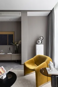 A modern living room featuring a yellow velvet armchair, side table with decorative items, and a sideboard with a vase and sc