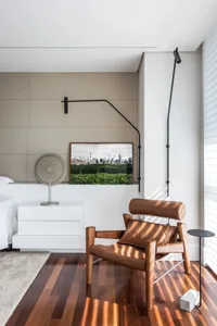A modern bedroom featuring a cozy brown leather chair with a pillow, positioned next to a wall-mounted lamp and a nightstand 