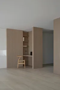A minimalist office space featuring a desk, chair, and shelves, with a focus on open space and natural light.