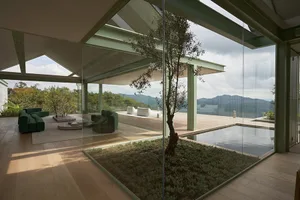 A panoramic view of a modern living room featuring glass walls and wooden flooring, with a pool and outdoor seating area.