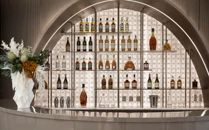 A modern metallic bar with a large arrangement of liquor bottles on a tiled wall.