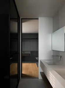 Modern minimalist bathroom featuring a white concrete double sink counter and a walk-in closet with grey walls.