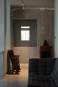 A minimalist living room with a concrete wall, grey sofa, and wooden chairs.