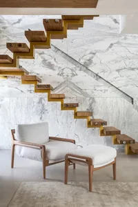 A modern interior space featuring a marble staircase with wooden steps and a white cushioned armchair and ottoman.