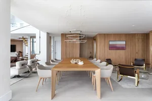 A minimalist dining room featuring a wooden table surrounded by white chairs and a geometric light fixture.