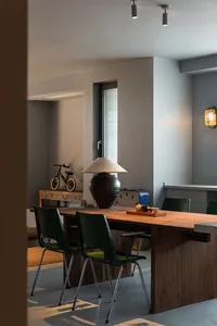 A modern dining room featuring a wooden table and chairs, set under natural light and adjacent to a window with blinds.