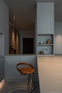 A minimalist residential kitchen featuring concrete countertops and a leather stool.