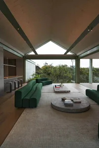 A modern living room with green fabric seating, wooden accents, and concrete elements.